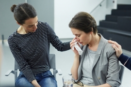 stressed-female-wiping-her-tears-with-paper-tissue-while-man-and-woman-comforting-her-SBI-324310458